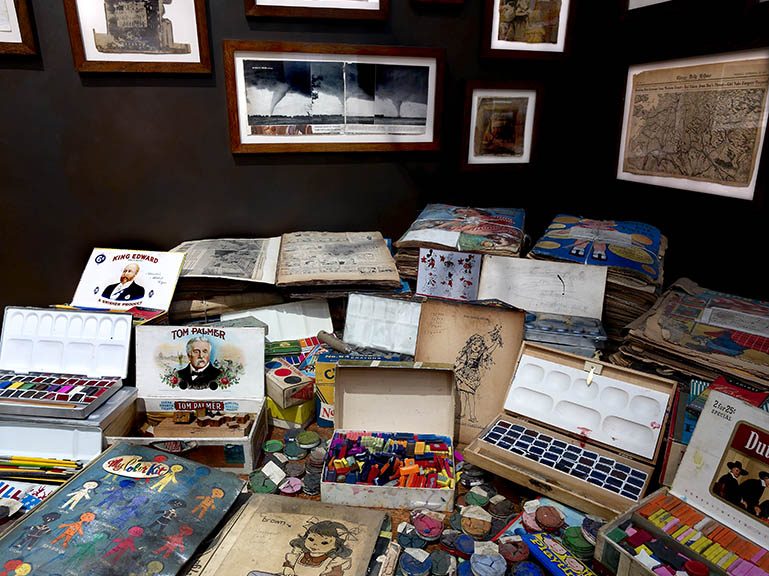 A zoomed in picture of a table with paint, children's coloring books and pastels on top of it.