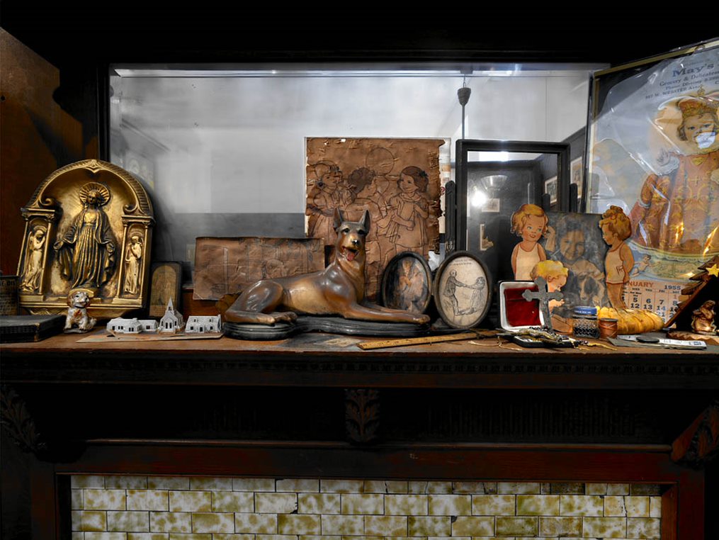 A zoomed in picture of a mantel. On the mantel is a dog figurine and drawings of a little girl with blonde hair.